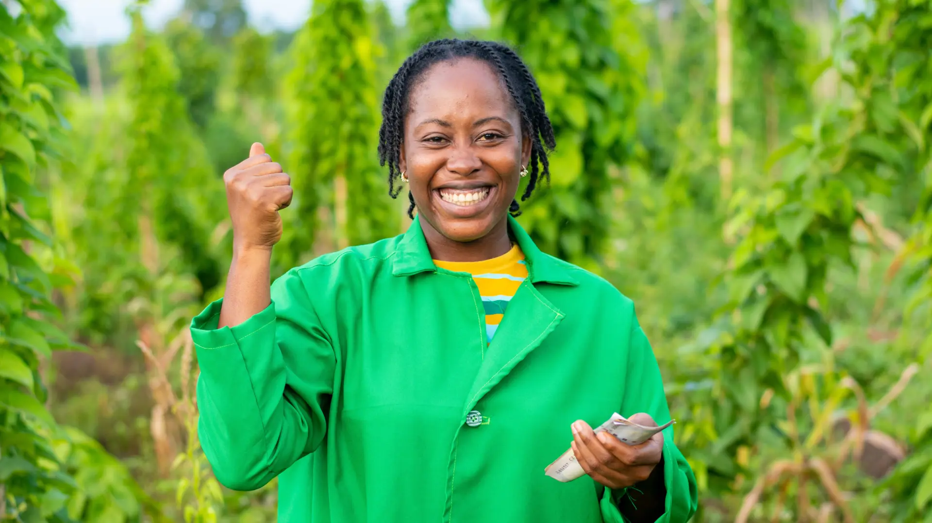 A smiling farmer in a green jacket in a field, holding banknotes after a sale